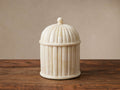 Jimena Lidded Jar, ivory bone inlay with fluted details, dome lid & finial, on a dark wooden table against a light wall.