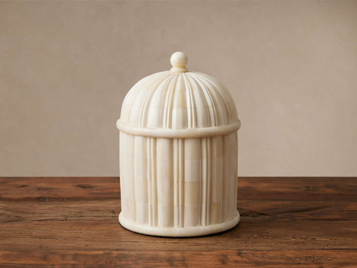 Jimena Lidded Jar, ivory bone inlay with fluted details, dome lid & finial, on a dark wooden table against a light wall.
