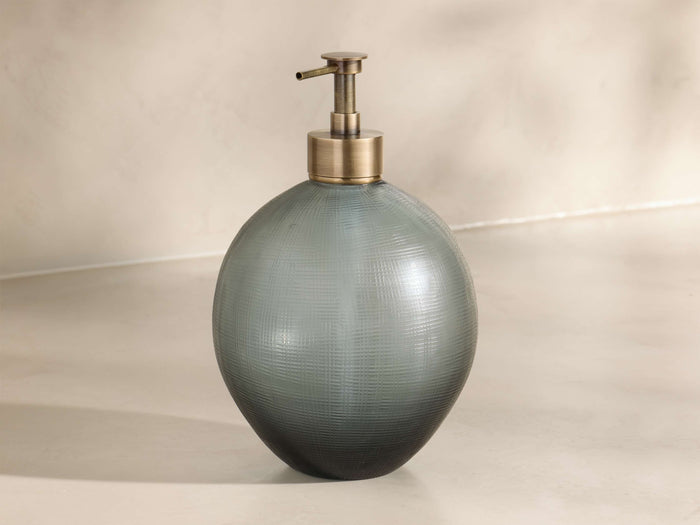 Front view of a round, muted teal glass soap dispenser with a subtle cross-hatch texture and an antique brass pump.