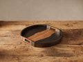Acacius Round Tray: dark oxidized steel frame, warm brown yukas wood inlay with organic edge and handles, on rustic wood.