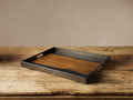 Acacius Tray. Rectangular tray with dark oxidized steel frame, warm brown yukas wood base, and cutout handles, on a rustic wood table.