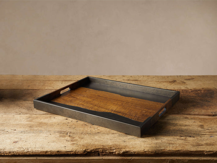 Acacius Tray. Rectangular tray with dark oxidized steel frame, warm brown yukas wood base, and cutout handles, on a rustic wood table.