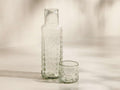 Front view of the clear textured Aera Carafe Set, featuring a tall carafe and a short tumbler with a bubbly pattern.