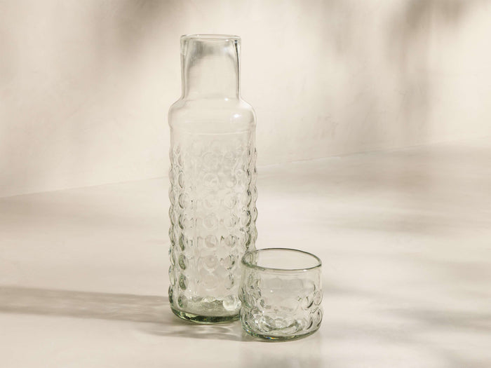 Front view of the clear textured Aera Carafe Set, featuring a tall carafe and a short tumbler with a bubbly pattern.