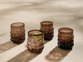 Four amber Aera Double Old Fashioned Glasses with a bubbly texture. One glass contains ice and a lime slice.