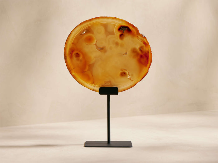 Circular Agate Slab in warm orange, brown, and translucent cream, with natural patterns, standing on a black powder-coated iron stand.