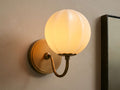 Agnes Gooseneck Sconce with antique brass base, curved arm, and glowing paneled cream glass globe shade mounted on a wall.