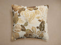 Square Alair Pillow with a woven floral leaf motif in cream, gold, and various brown shades, centered on a light background.