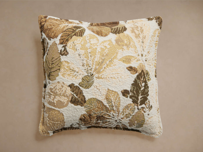 Square Alair Pillow with a woven floral leaf motif in cream, gold, and various brown shades, centered on a light background.