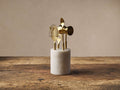 Front view of the gold Alexandria Cocktail Tool Set: bottle opener, bar spoon, peg measurer, and strainer in a white marble holder.