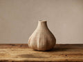 Natural handwoven Allium Basket, beige, gourd-shaped with a narrow neck, on a weathered wooden table.