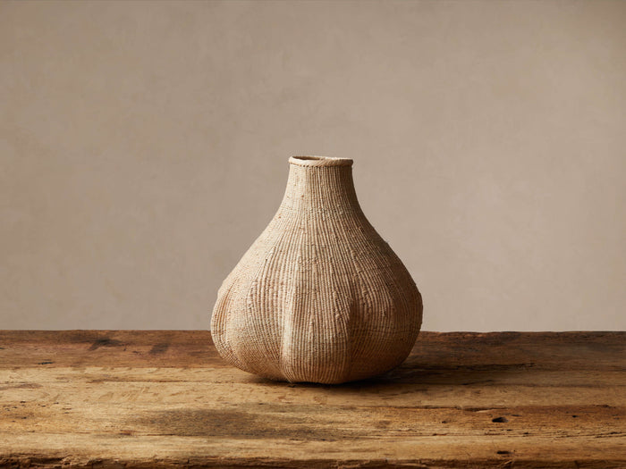 Natural handwoven Allium Basket, beige, gourd-shaped with a narrow neck, on a weathered wooden table.