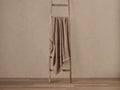 Speckled light brown Alpaca Boucle Throw with fringe draped over a rustic wooden ladder against a beige wall.