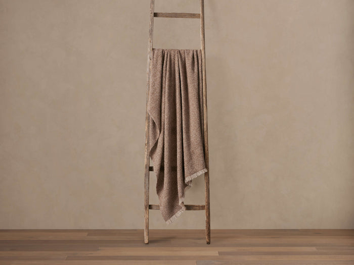 Speckled light brown Alpaca Boucle Throw with fringe draped over a rustic wooden ladder against a beige wall.