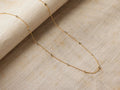 Alvita Necklace: Delicate gold-plated sterling silver chain with evenly spaced, bezel-set, light gray rose-cut diamonds, on a textured beige surface.