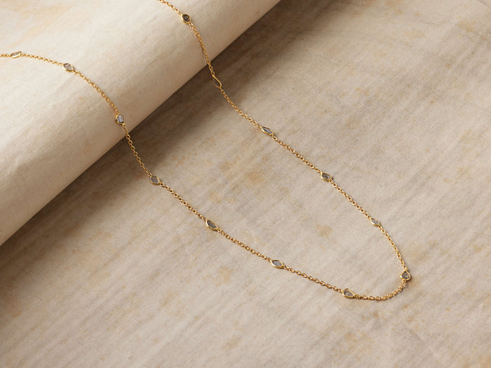 Alvita Necklace: Delicate gold-plated sterling silver chain with evenly spaced, bezel-set, light gray rose-cut diamonds, on a textured beige surface.