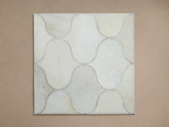 Amberly Rug Swatch: Square hair-on-hide sample with stitched, interlocking wavy cream and light grey shapes, laid flat.