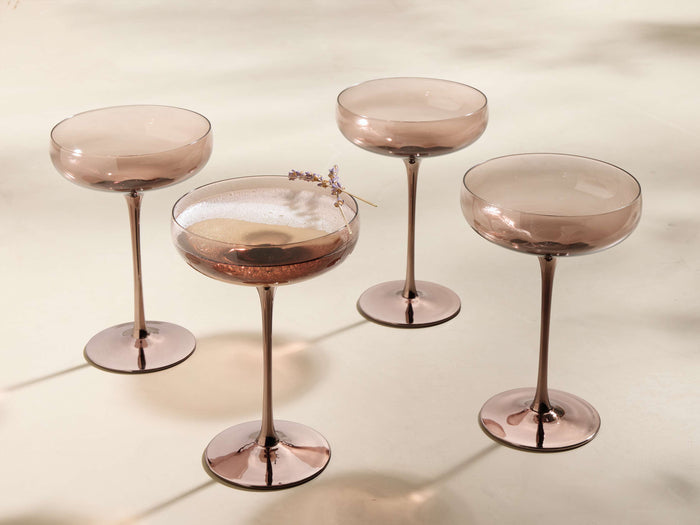 Front view of four Ambretta Coupe Glasses with mocha-smoke glass bowls and metallic bronze stems and bases. One holds a drink with lavender.