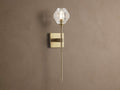 Amoroso Sconce: brass-plated wall light with long rod and illuminated faceted clear crystal shade on a brown wall.