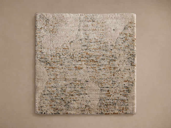 Anala Rug Swatch in light beige with textured surface and speckled pattern featuring grey and brown tones, on a neutral backdrop.
