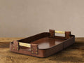Andres Leather Tray, rectangular, rich brown buffalo hide with antiqued brass handles, resting on a rustic wood surface.