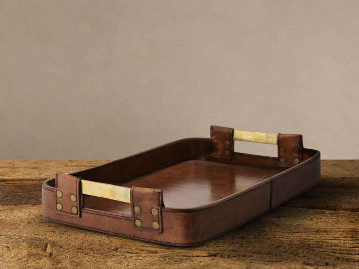 Andres Leather Tray, rectangular, rich brown buffalo hide with antiqued brass handles, resting on a rustic wood surface.