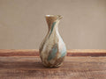 Andromeda Pitcher, mouth-blown glass with organic curves and swirling brown, beige, and teal colors on a wooden table.