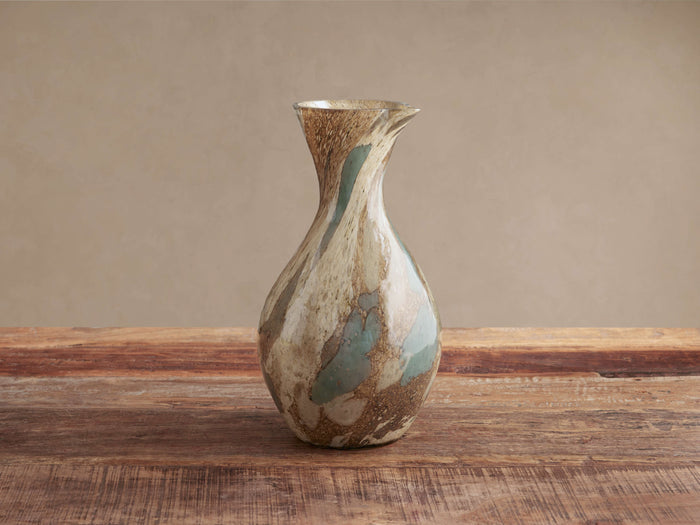 Andromeda Pitcher, mouth-blown glass with organic curves and swirling brown, beige, and teal colors on a wooden table.