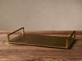 Angelo Rectangular Tray in antique brass aluminum, shown at an angle on a wooden surface, with raised, rectangular handles.