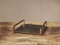 Angelo Square Tray: square, antique brass finish aluminum tray with two raised handles, on a rustic wood table.