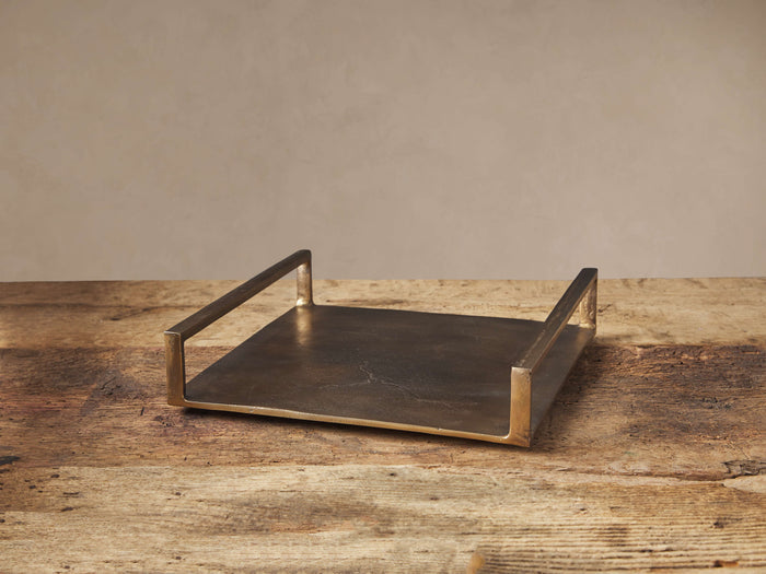 Angelo Square Tray: square, antique brass finish aluminum tray with two raised handles, on a rustic wood table.