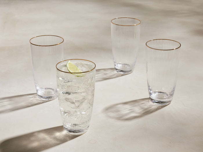 Set of 4 Anisa highball glasses: clear ribbed glass with gold rims. One has ice, liquid & lime; 3 are empty.