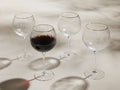 Front view of four clear Anisa Red Wine Glasses with ribbed bowls and gold rims, one filled with red wine.