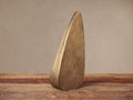 Abstract, curved antique brass sculpture with textured finish stands on rustic wood surface.