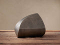 Curved antique nickel sculpture in dark metallic gray, with a smooth, abstract shape, on a rustic wooden surface.