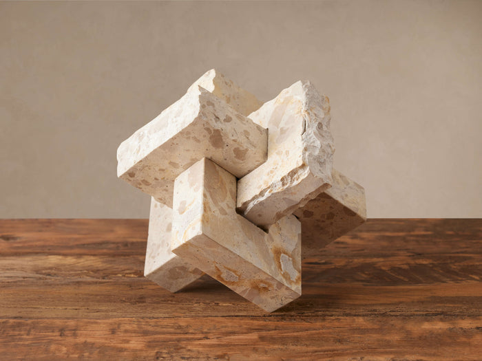 Aphra Abstract Sculpture: geometric interlocking blocks of natural, rough-edged beige and ivory mottled marble on a wooden surface.