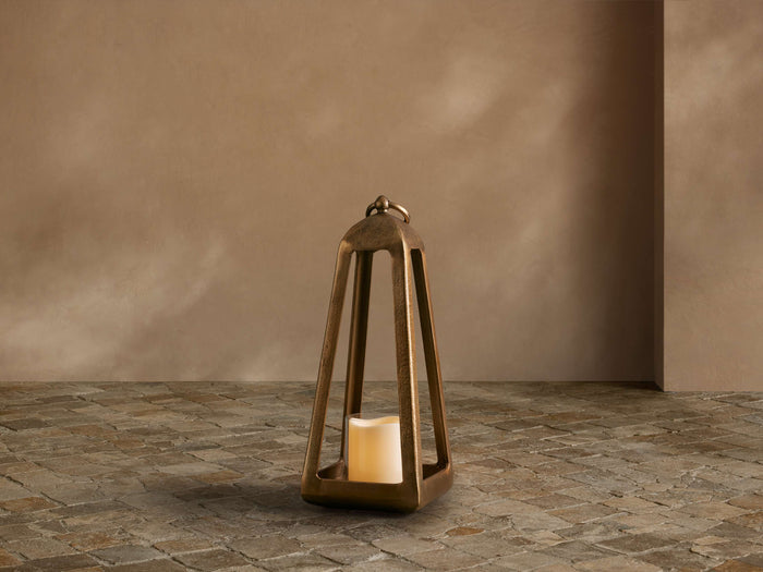 Bronze-finished Arc Lantern with a flameless candle inside, on a cobbled floor against a warm taupe wall.