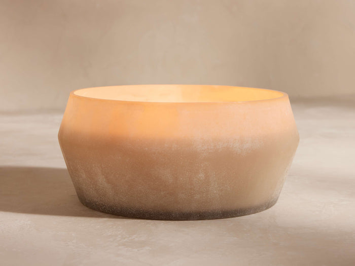 Arhaus Elements Coastline candle in a textured, bowl-shaped frosted glass holder, light beige fading to dark, with a warm glow.