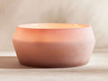 Arhaus Elements Candle in Dawn: Wide, frosted glass holder, rosy pink at base, fading to light peach at the top, on a neutral surface.