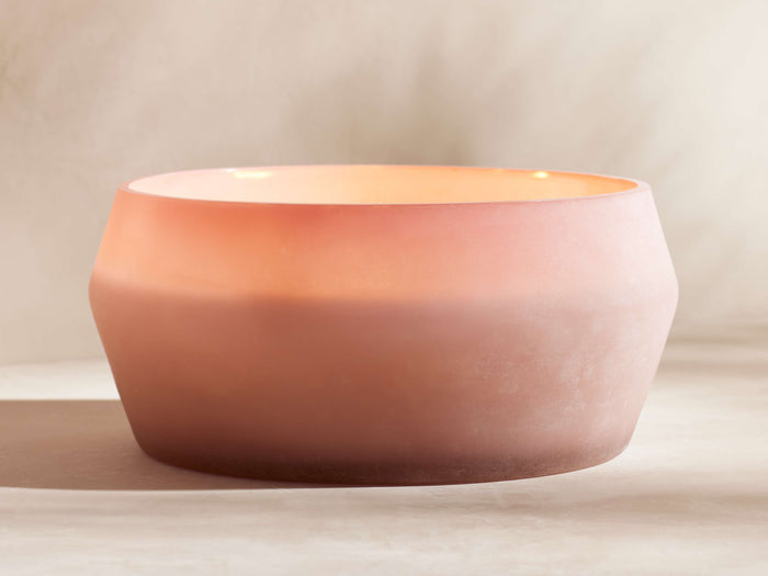Arhaus Elements Candle in Dawn: Wide, frosted glass holder, rosy pink at base, fading to light peach at the top, on a neutral surface.