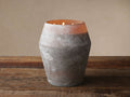 Arhaus Elements Eventide candle in a wide, distressed gray-brown frosted glass vessel with 3 lit wicks, casting an orange glow on wood.