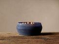 Arhaus Elements Candle in Thunder: Wide, dark blue frosted glass vessel with several lit wicks on rustic wood.
