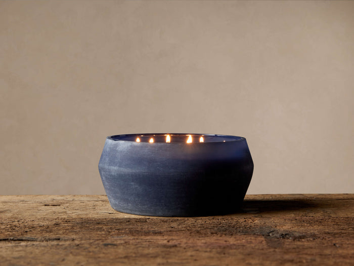 Arhaus Elements Candle in Thunder: Wide, dark blue frosted glass vessel with several lit wicks on rustic wood.