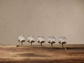Artemis Multi Candle Holder. Horizontal antique brass stand holds 5 lit tealights in clear glass globes on a rustic wood table.