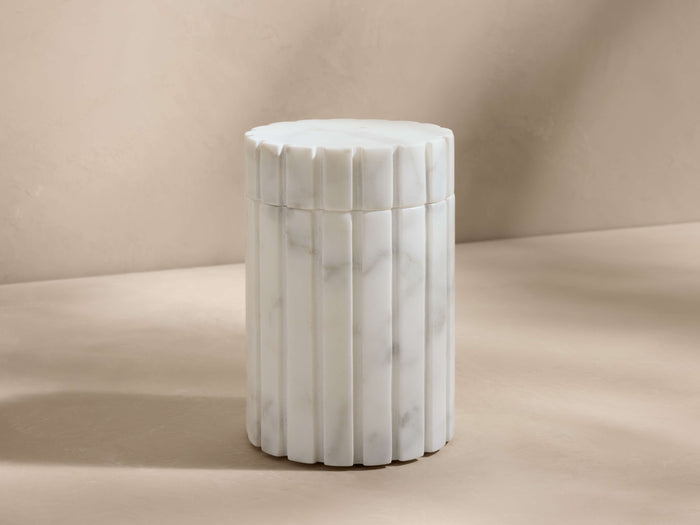 A cylindrical canister with ribbed texture and marble-like Carrara finish, featuring a removable lid, on a beige background.