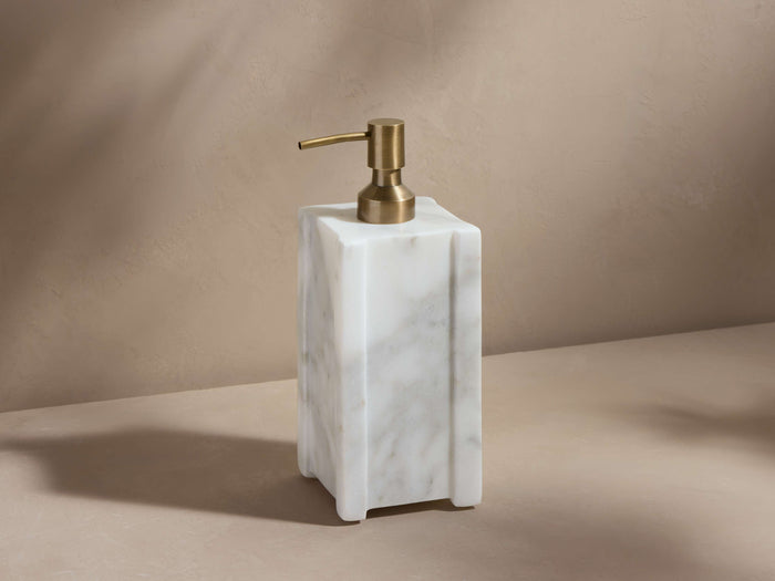 A white Carrara marble soap dispenser with natural veining, featuring an antique brass metal pump, on a neutral background.