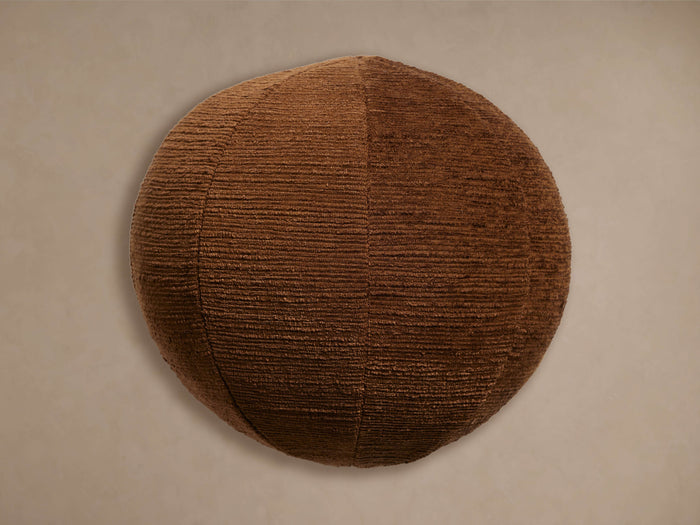 Atwood Sphere Pillow, a round dark brown pillow with ribbed, textured fabric, centered against a neutral wall.