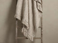 Light beige chunky knit throw blanket with bobble texture and fringed edges, casually draped over a rustic wooden ladder.