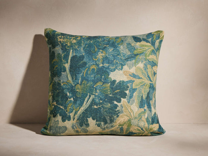 Square Audra Pillow with a dense blue, green, and cream botanical pattern, angled on a soft neutral background.