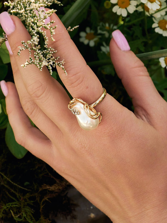 Gold ring with a pearl on a hand against a natural background